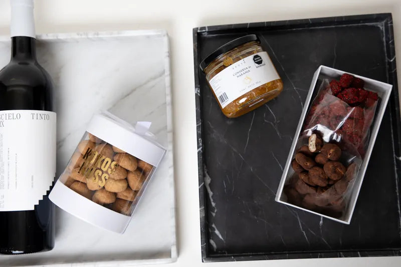 Charolas de mármol blanco y negro con vino y repostería