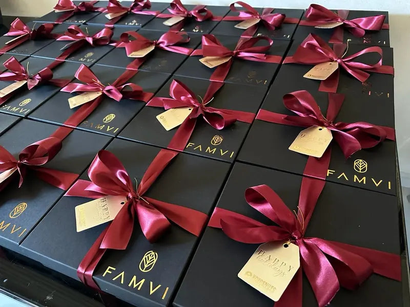 Cajas negras con logo dorado de FAMVI y moños vino