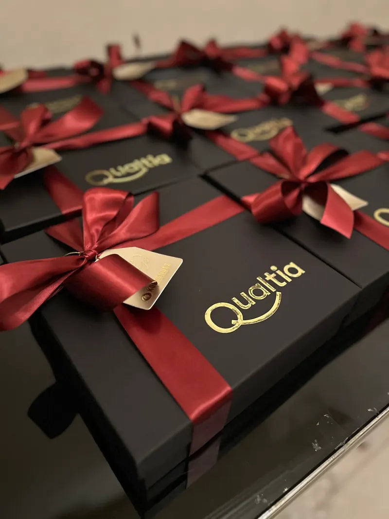 Cajas negras con logo dorado de Qualtia y moño vino