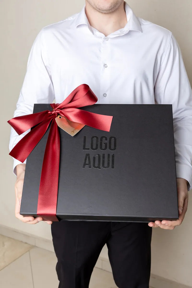 Persona sosteniendo una caja rígida negra con logo y moño vino